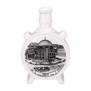 May include: White ceramic flask featuring a black and white illustration of a domed building. The flask has a rounded body, a cylindrical neck, and three small feet. The text "PECS SZECHENYI TER" is printed on the flask.