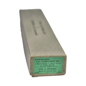 Könnte beinhalten: Eine Vintage-Box für das FLOWERTIME 5-teilige BESTECK-SET. Die hellbraune Box hat ein grünes Etikett mit dem Inhalt: Buttermesser, Zuckerlöffel, Esslöffel und ein durchbrochener Esslöffel. Hergestellt von WM. A. ROGERS®.