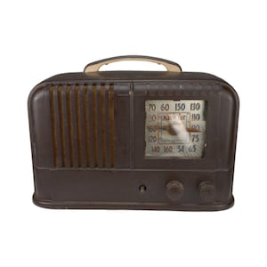 May include: A vintage brown radio with a cream-colored handle. The radio has a speaker grill on the left side and a clear dial with numbers and a needle. Two knobs are visible on the front.