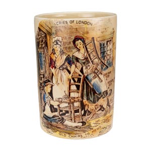 May include: A cylindrical ceramic mug with a vintage illustration depicting scenes of London street life. The mug features figures mending chairs, with text that reads "Cries of London" and "Old Chairs to Mend."