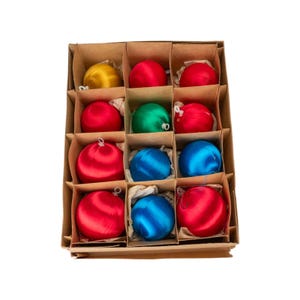 May include: A vintage box of Christmas ornaments. The box is divided into compartments, each holding a satin-like sphere in various colors: gold, red, green, and blue. The ornaments are round and have a shiny finish, suggesting a classic holiday decoration.
