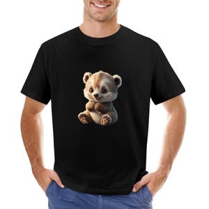 May include: Black t-shirt featuring a cartoon illustration of a cute, seated bear cub. The bear cub has brown and cream-colored fur and is smiling. The t-shirt is made of a soft material.