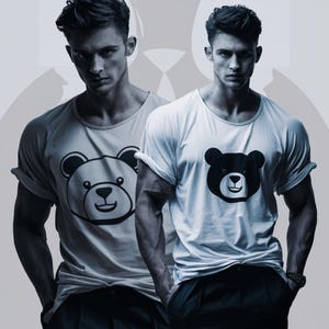 May include: Two men wearing white t-shirts with a black bear face graphic. The t-shirts have rolled-up sleeves and are paired with black pants. The background is a light gray color.