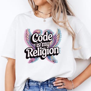 Może przedstawiać: Biała koszulka z napisem "Code is my Religion" w stylizowanej czcionce, z grafiką skrzydeł w odcieniach różu, błękitu i fioletu. Koszulka jest połączona z niebieskimi dżinsami.