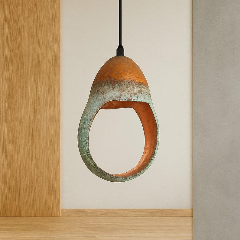 Może przedstawiać: Lampa wisząca w kształcie kropli. G&oacute;rna część jest pomarańczowa, przechodząca w turkusowy pas, z miedzianym wnętrzem. Wisi na czarnym kablu, prezentując nowoczesny, artystyczny design, idealny do wnętrz.