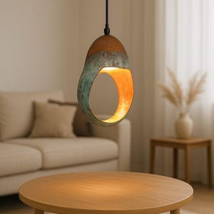 Może przedstawiać: Nowoczesna lampa wisząca o unikalnym, otwartym designie. Lampa ma brązową g&oacute;rę, przechodzącą w turkusowo-zieloną środkową część i ciepłe pomarańczowe wnętrze. Wisi na czarnym kablu, oświetlając przestrzeń mieszkalną.