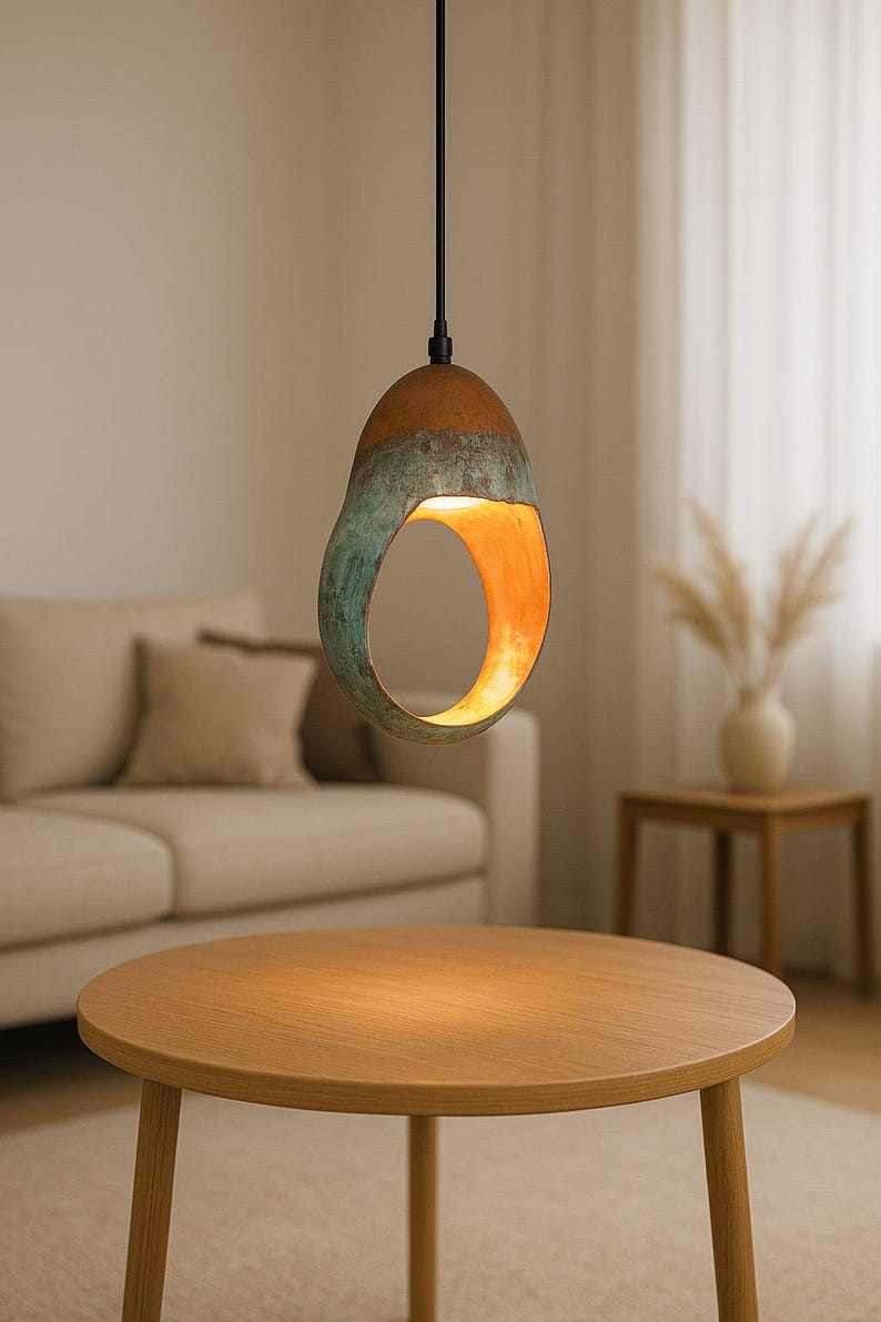 Może przedstawiać: Nowoczesna lampa wisząca o unikalnym, otwartym designie. Lampa ma brązową g&oacute;rę, przechodzącą w turkusowo-zieloną środkową część i ciepłe pomarańczowe wnętrze. Wisi na czarnym kablu, oświetlając przestrzeń mieszkalną.