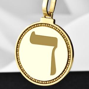 May include: A gold-colored pendant necklace featuring a circular pendant with a stylized letter. The pendant hangs from a matching gold rope chain. The pendant has a beaded border and a polished finish.