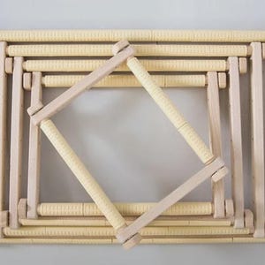 Puede incluir: Un conjunto de bastidores de bordado rectangulares encajables fabricados en madera clara. Cada bastidor cuenta con cuatro barras cilíndricas con una superficie de agarre texturizada de color crema, unidas por piezas de esquina de madera.