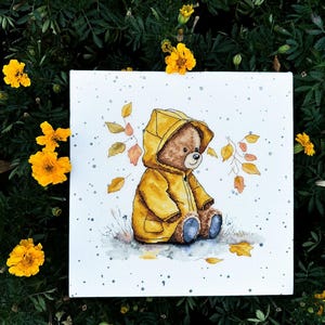 May include: A cross-stitch pattern of a brown teddy bear wearing a yellow raincoat and sitting on a white background with scattered gray and blue dots. The bear is surrounded by brown branches with yellow leaves.