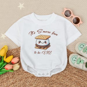 May include: White baby onesie with a cartoon s'more graphic and the text "It's S'more fun to be ONE".