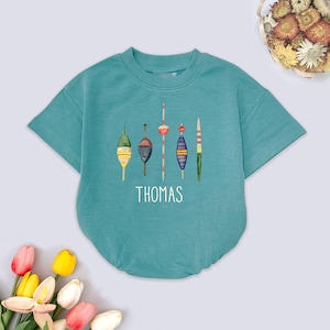 May include: Teal-colored baby romper with a crew neck and short sleeves. The front features a watercolor illustration of five fishing bobbers in various colors. The name "THOMAS" is printed in white below the bobbers.