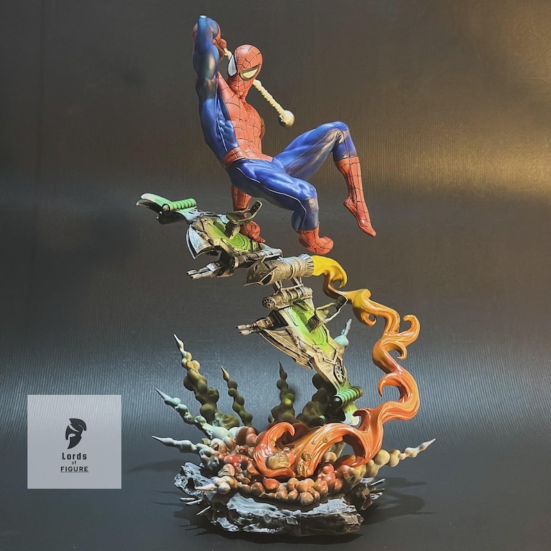 Op de afbeelding: Een rood en blauw Spiderman-actiefiguur is in de lucht geposeerd, zwaaiend aan een web, op een groen en grijs ruimteschip-achtig voetstuk. Het voetstuk is omgeven door oranje en gele vlammen en groen en grijs gebladerte.