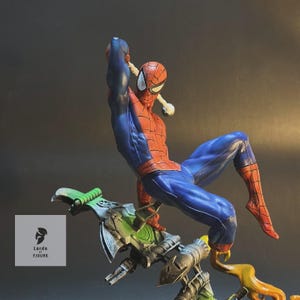 Op de afbeelding: Een rood en blauw Spider-Man-actiefiguur is geposeerd in een dynamische actiehoud, rijdend op een groene en grijze zweefvliegtuig met vlammen die uit de achterkant komen. De figuur maakt deel uit van een Lords of Figure-collectie.