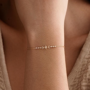 Puede incluir: Una delicada pulsera dorada con un diseño celestial. La pulsera presenta un motivo central de estrella, flanqueado por medias lunas y pequeños acentos brillantes. La fina cadena y los intrincados detalles crean un accesorio elegante.