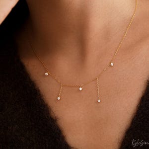 May include: A delicate gold chain necklace featuring five small, clear, round-cut stones set in gold. Two of the stones are suspended from the main chain on short gold links, while the other three are integrated directly into the chain.