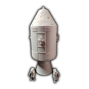May include: White 3D printed model of a space capsule with two astronauts standing in front of it.