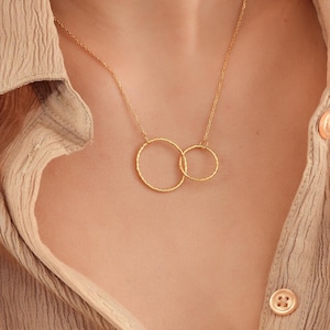 May include: A gold necklace with two interlocking circles. The circles are textured and have a hammered finish.