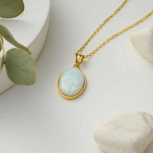 May include: A gold chain necklace with a white oval opal pendant.
