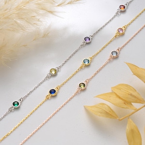 May include: Four delicate bracelets with colorful gemstones. The bracelets are in silver, gold, and rose gold tones. Each bracelet features a chain with round, bezel-set gemstones in various colors, including green, blue, yellow, and purple.