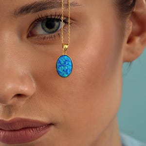 May include: A gold chain necklace with a blue oval opal pendant. The pendant is set in a gold frame and has a shimmering blue and green color.