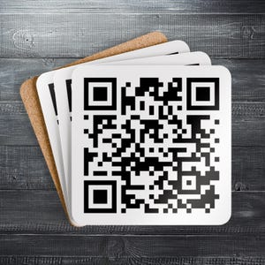 Op de afbeelding: Een stapel vierkante onderzetters met een QR-code ontwerp. De onderzetters hebben een wit oppervlak met een zwart-witte QR-code en een natuurlijke kurken achterkant. Ze zijn gerangschikt op een donkergrijze houten ondergrond.