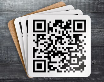 May include: A stack of square coasters with a QR code design. The coasters have a white surface with a black and white QR code and a natural cork backing. The coasters are arranged on a dark gray wooden surface.