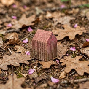 以下が含まれることがあります： 切妻屋根の形をした小さな木製のブロック。木材には自然な木目があり、表面には色あせたピンク色のステインが塗られており、前面と側面に目に見える質感と垂直の線がはっきりと現れています。