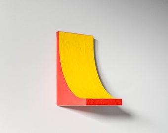May include: A red and yellow abstract sculpture with a curved shape. The sculpture is made of painted wood and has a smooth, glossy finish.