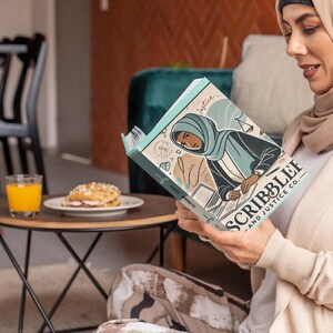 May include: A person wearing a beige headscarf is reading a teal and white book titled "Scribble & Justice Co.". The book features an illustration of a woman wearing a blue headscarf and a black robe.