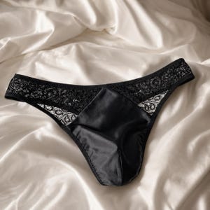 May include: Black underwear featuring a smooth satin front panel and a wide waistband made of intricate black floral lace. The design includes a high-cut leg opening and a seamless transition between the satin fabric and the lace detailing.