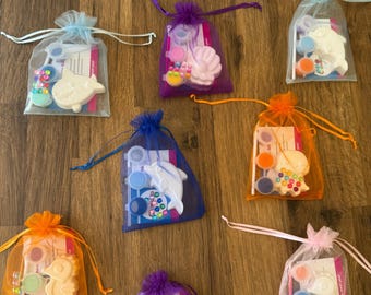 Könnte beinhalten: Eine Sammlung kleiner, durchsichtiger Beutel mit Kordelzug in verschiedenen Farben, die jeweils ein Mal-dich-selbst-Bastelset enthalten. Die Sets enthalten Meerestiere wie Delfine, Seepferdchen und Muscheln sowie Farbtöpfe und Perlen. Das Wort "CHERISHED" steht auf einer Karte.
