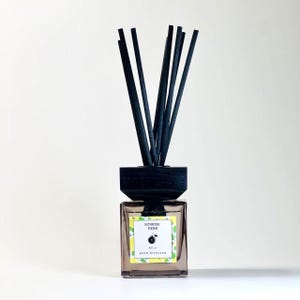 May include: A square glass reed diffuser with black reeds. The label reads "Sunrise Herb No. 3 Reed Diffuser" with a lemon and leaf design. The diffuser has a dark wooden top and is set against a white background.