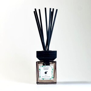 May include: A square glass reed diffuser bottle with a dark wooden cap and black reeds. The label reads "Twilight Jasmine" and "No. 5 Reed Diffuser" with a small fruit illustration. The bottle contains a light brown liquid.