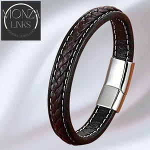 Könnte beinhalten: Dunkelbraunes Lederarmband mit geflochtener Mitte und weißen Nähten. Das Armband hat einen silbernen Magnetverschluss. Das Logo "MONZA LINKS MODERN JEWELLERY" befindet sich in der oberen linken Ecke.
