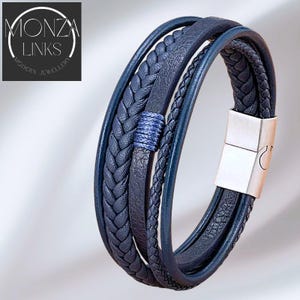 May include: A multi-strand blue leather bracelet with a silver clasp. The bracelet features braided and smooth leather strands, with a wrapped blue accent. The brand name "MONZA LINKS MODERN JEWELLERY" is in the upper left corner.
