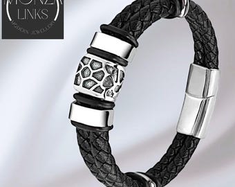 May include: Black braided leather bracelet with silver metal detailing. The bracelet has a central decorative section with a geometric design. The text "MONZA LINKS MODERN JEWELLERY" is in a circular logo.