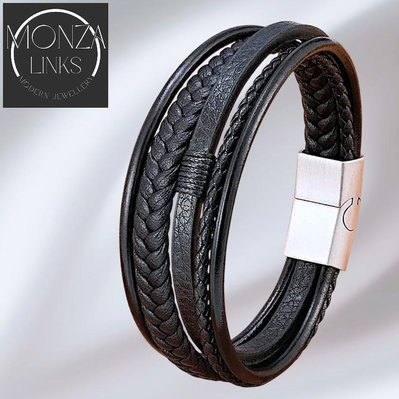 Puede incluir: Pulsera de cuero negro con m&uacute;ltiples hebras, incluyendo texturas trenzadas y lisas. La pulsera presenta un cierre magn&eacute;tico de color plateado. La marca "MONZA LINKS MODERN JEWELLERY" es visible en la esquina superior izquierda.