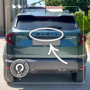 Puede incluir: Vista trasera de un SUV Dacia Duster de color verde oscuro con un emblema Dacia negro centrado en el portón trasero. El vehículo incluye un limpiaparabrisas trasero, luces traseras rojas, un parachoques gris oscuro y un soporte de matrícula.