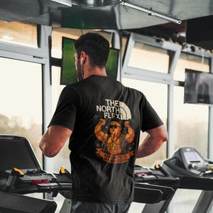 May include: A person wearing a black t-shirt with a graphic of a muscular man with the text "The North Flex" and "Strength is Mandatory". The person is running on a treadmill in a gym.