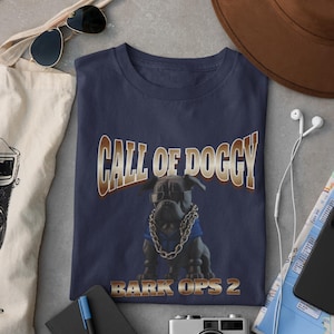 Könnte beinhalten: Ein marineblaues T-Shirt mit einem Grafikdruck eines Cartoon-Hundes, der eine Sonnenbrille und eine goldene Kette trägt. Der Text "Call of Doggy Bark Ops 2" ist auf dem Shirt aufgedruckt.