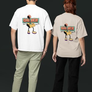 Può includere: Due persone indossano magliette bianche e beige con una grafica retrò da giocatore sul retro. La grafica presenta un joystick con il testo "Gamer Since Day One".