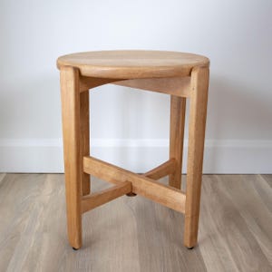 Peut inclure: Un tabouret en bois clair avec une assise ronde et quatre pieds droits. Les pieds sont reliés par un support en forme de croix près de la base. Le tabouret est en bois clair et présente un design simple et minimaliste.