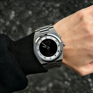 May include: A silver-toned wristwatch with a metallic link band and a circular face. The watch features a black center dial surrounded by a white outer ring marked with black Japanese kanji numerals. Two silver hands indicate the time.