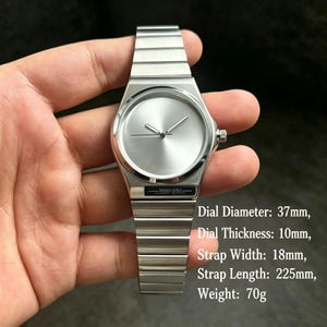 May include: A silver wristwatch with a minimalist design. The watch features a round face with a simple dial and a metallic band. The dial diameter is 37mm, thickness is 10mm, strap width is 18mm, strap length is 225mm, and the weight is 70g.