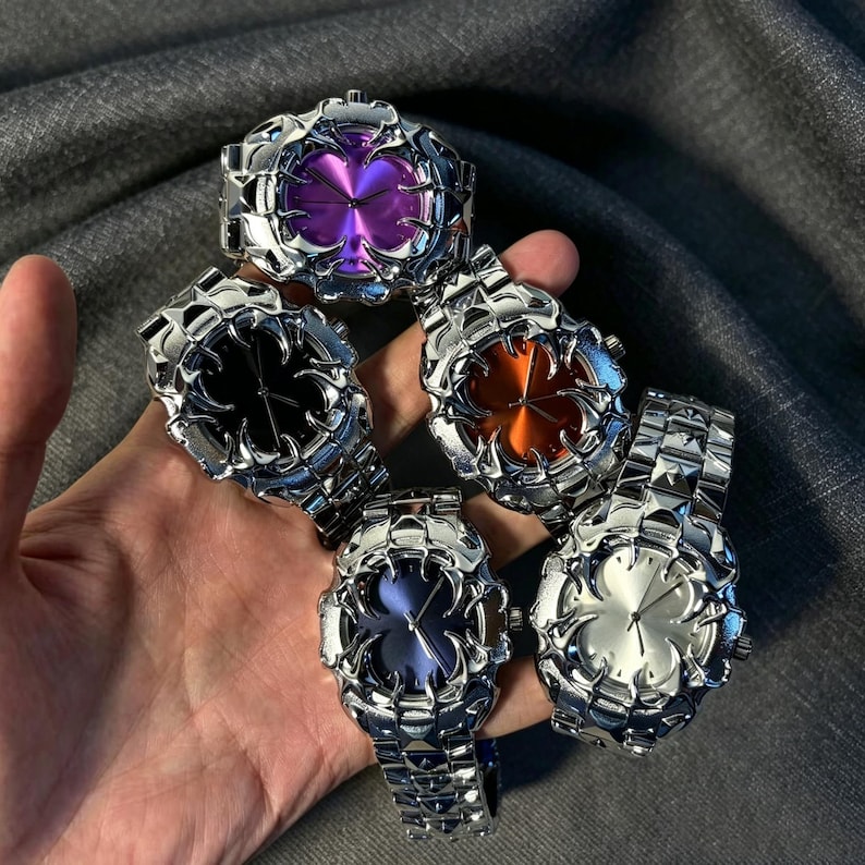 May include: Five silver-toned wristwatches with unique, textured designs. Each watch features a different colored face: purple, black, orange, blue, and silver. The watches are held in a hand, showcasing their intricate details.