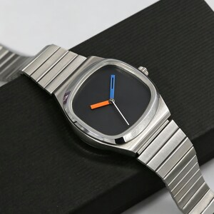 May include: A stainless steel wristwatch with a square black face. The watch features a silver band and orange and blue hands. The watch is displayed on a black surface.