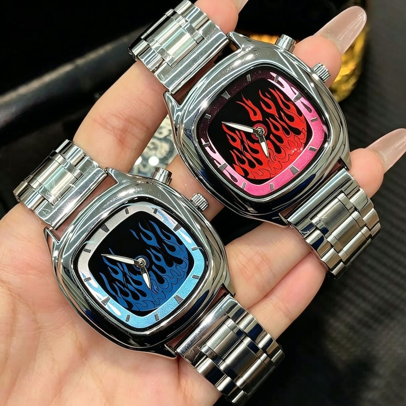 May include: Two silver-toned metal wristwatches with square-rounded cases and link bracelets. One watch features a black dial with blue flame graphics, while the other displays a black dial with red flame graphics. Both have silver hands.