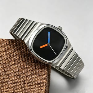 May include: A modern wristwatch with a silver-tone metal band and a black square watch face. The watch face features blue and orange accent markers and a white second hand. The watch is displayed on a brown textured surface.