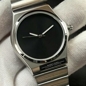 May include: A stainless steel wristwatch with a black face and silver hands. The watch has a minimalist design with the text "NIRUISI QUARTA WATCH" on the band. The watch is on a silver metal band.